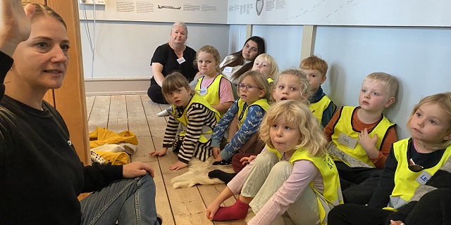 Børn fra Børnehuset Solstrålen sidder på gulvet og lytter til museumsformidler Marie Abel Hesse. Foto: Mikala Tordrup